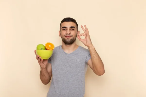 Man holding a bowl of fresh fruit and giving an OK sign representing the role of proper nutrition during tirzepatide treatment