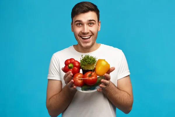 Man in white t-shirt smiling while holding a bowl of fresh vegetables