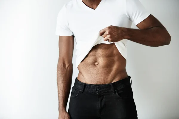 Man lifting shirt to reveal toned abdominal muscles after abdominoplasty surgery