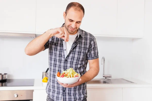 Man preparing a fresh salad with lettuce and tomatoes in his kitchen, showcasing healthy foods that speed up post-surgery recovery