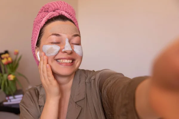 Woman with pink hair towel gently touching her face during skincare routine
