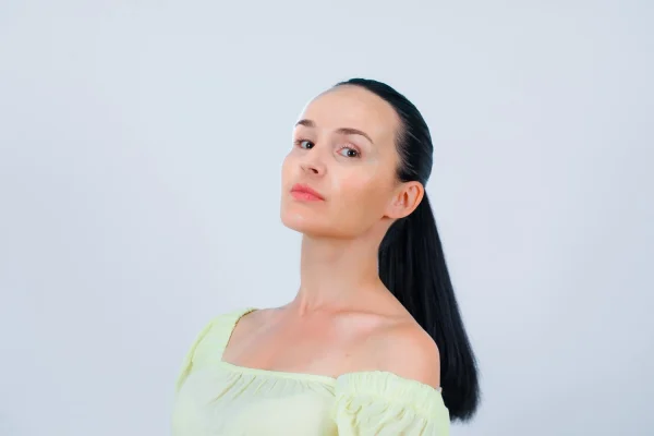 Woman with sleek dark hair in a ponytail wearing an off-shoulder yellow top