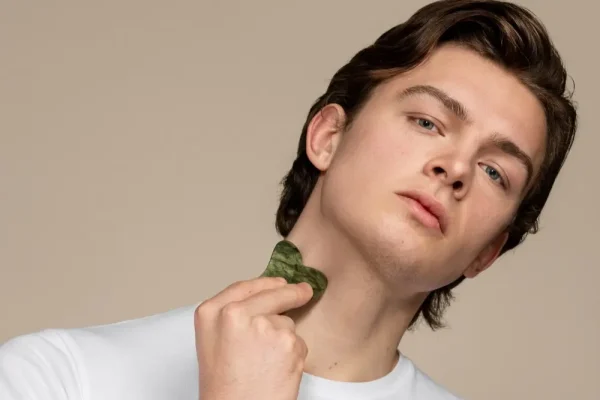 Young man using a gua sha tool on his neck to promote skin firming and maintain a smooth, taut jawline