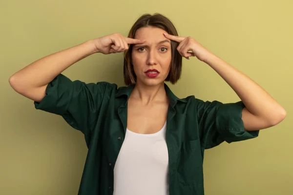 Confident pretty woman puts fingers on forehead isolated on olive green wall