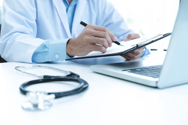 Doctor working with laptop computer and writing on paperwork