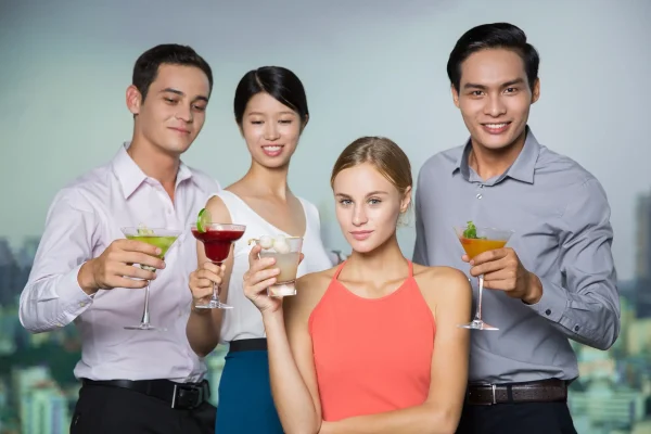 Four smiling young people holding cocktails in bar