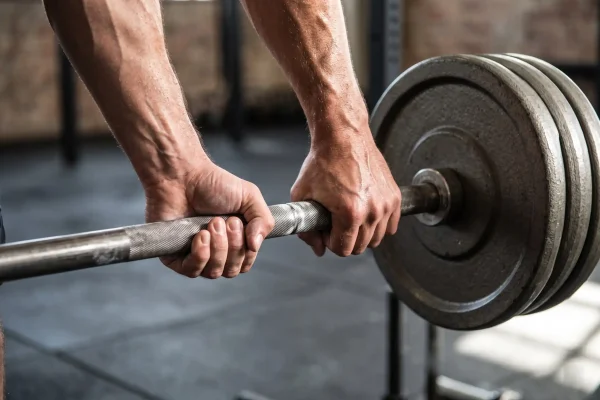 Hands gripping a barbell, showing resistance training that protects muscle during fat loss