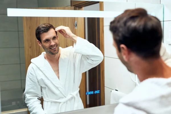 Reflection in a mirror of happy man in bathrobe adjusting his hairstyle after prp