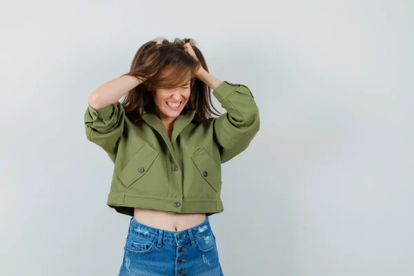 young girl tearing her hair in jacket, shorts and looking excited. Front view.