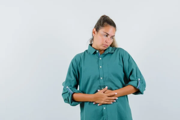 Young woman in blue shirt holding hands on her belly and looking tedious