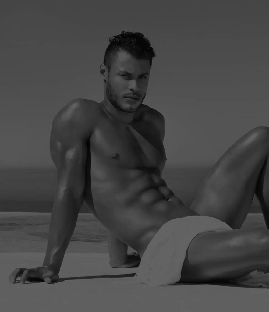 male model sitting, posing with beach with towel on lap after plastic surgery recovery