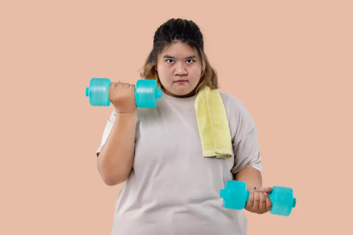 Person holding turquoise dumbbells with yellow towel around neck demonstrating strength training exercise for stable weight maintenance before tummy tuck surgery.