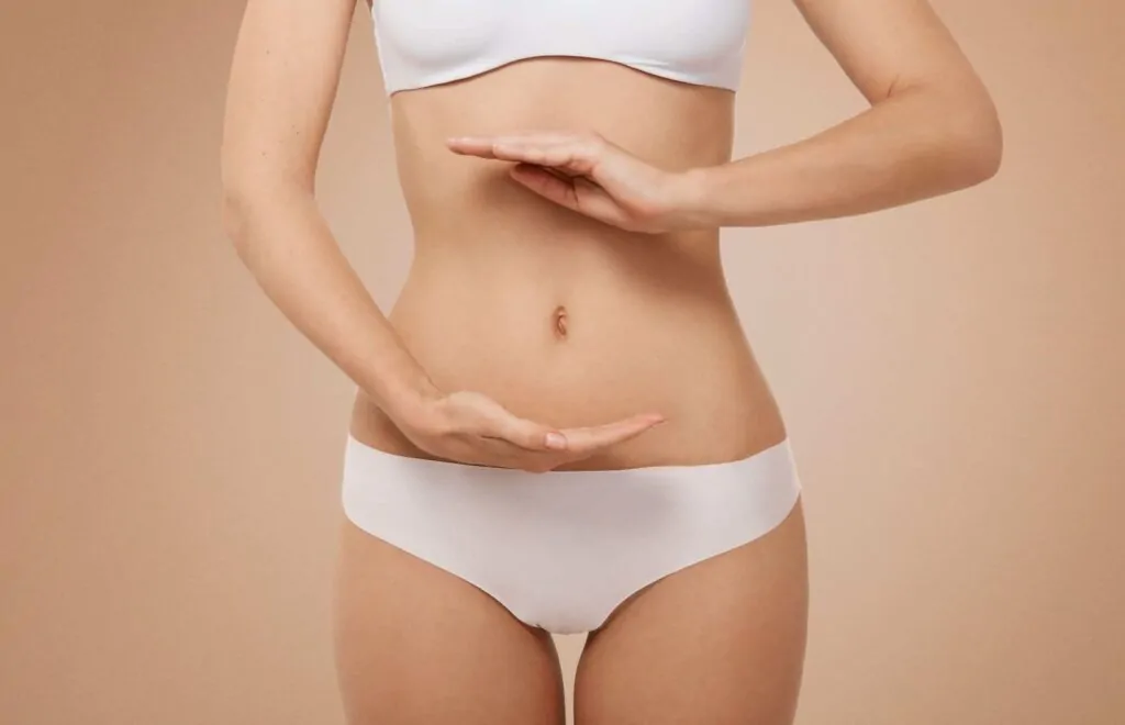 Fit woman wearing white lingerie showing belly button after plastic surgery