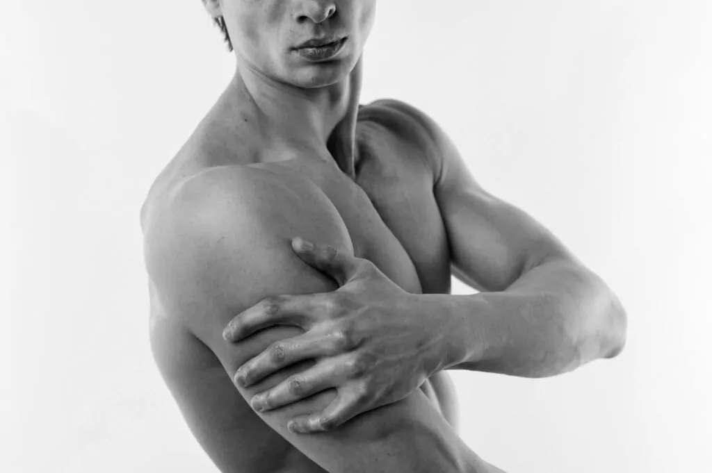 Black and white artistic photograph showing sculpted chest and arm definition, illustrating body contouring results from liposuction techniques