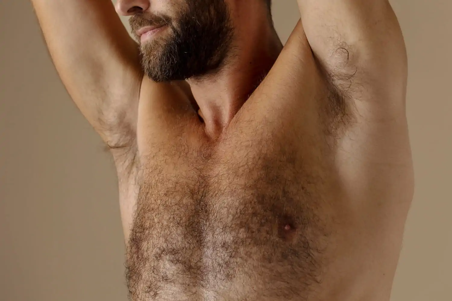 Close-up of a bearded man with both arms raised, showing his underarm and chest area, illustrating the treatment zone to prepare before and care for after underarm Botox injections.