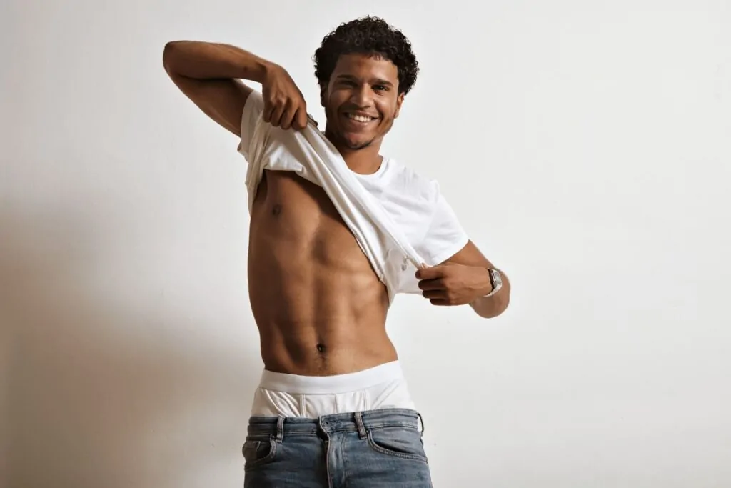 Fit man lifting shirt to reveal toned, scar-free abdomen after HD liposuction procedure