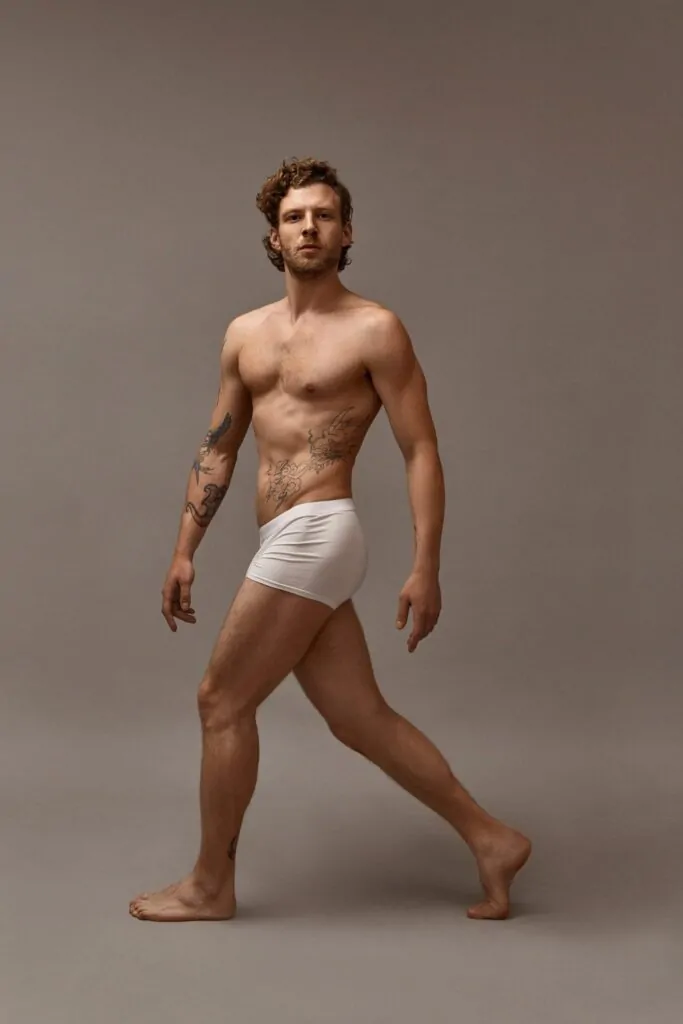 Full length shot of fit attractive tattooed man with muscular perfect body walking isolated wearing white boxer shorts