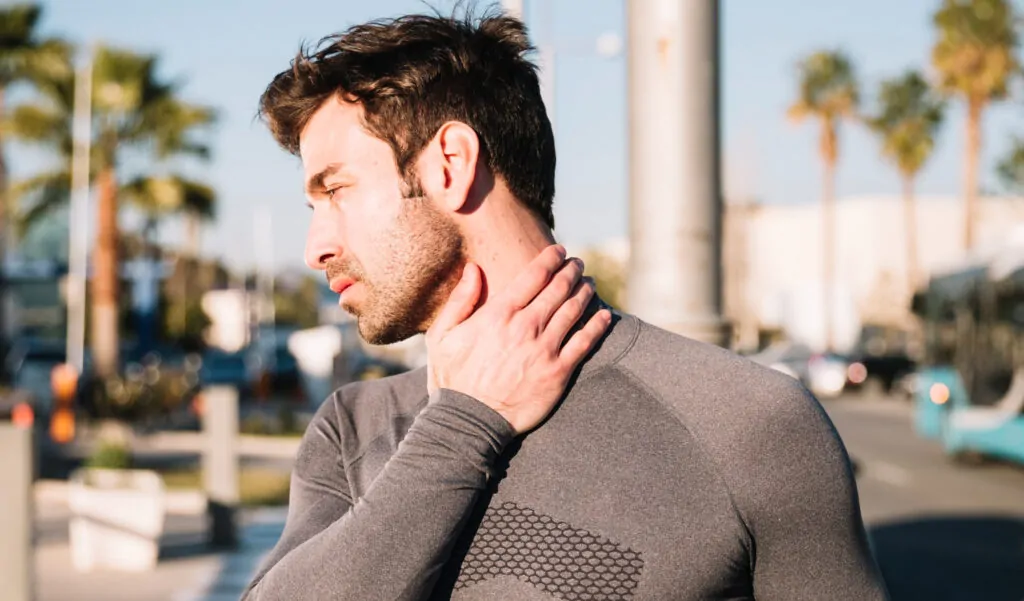 Man holding neck outdoors with palm trees, depicting PDO thread lift treatment area for neck rejuvenation in Tampa, FL