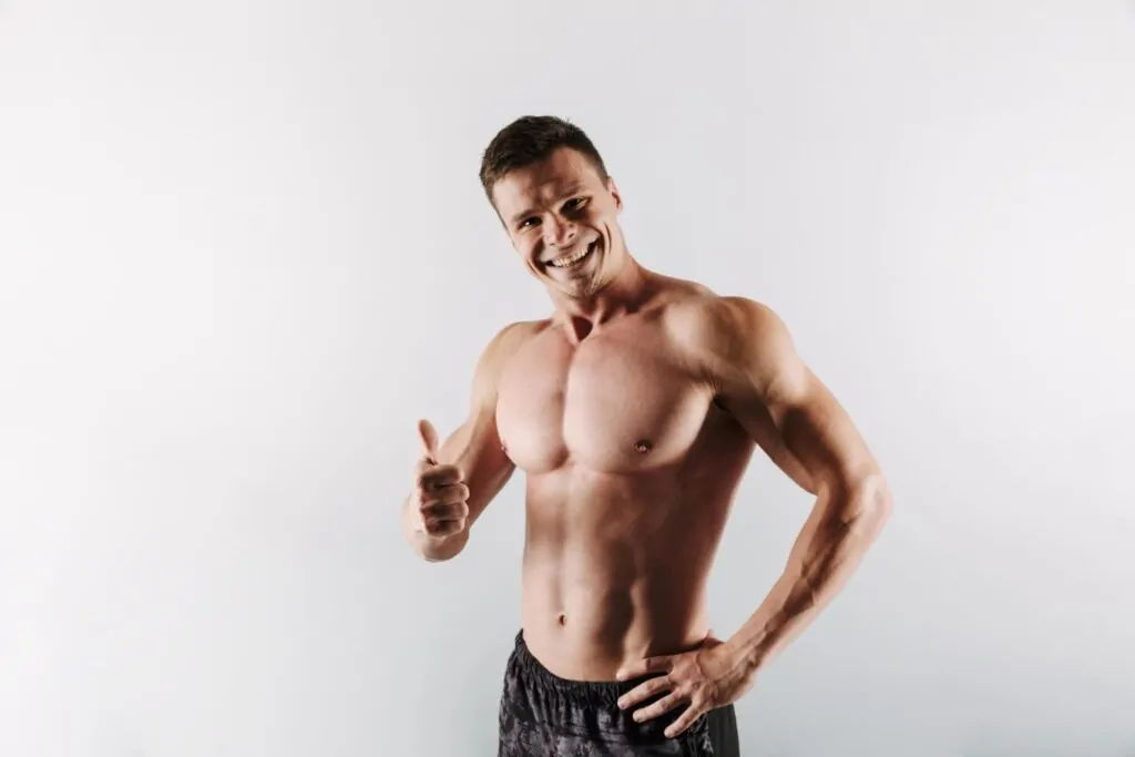 Smiling shirtless muscular man giving a thumbs up, emphasizing the positive outcomes of following safe peptide usage guidelines for muscle growth.