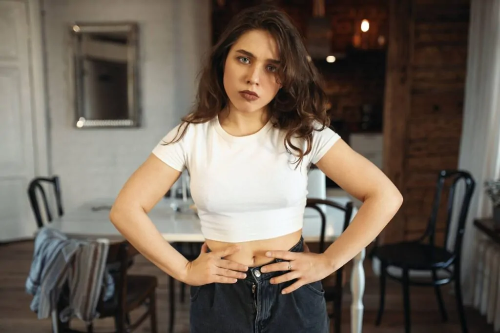 A young woman in a white crop top and jeans stands with hands on her hips