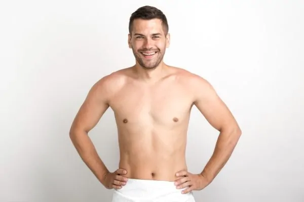 Happy shirtless man posing against white wall after full body liposuction