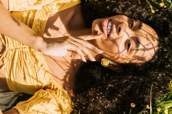 A woman lying on the grass, flexing her face after plastic surgery