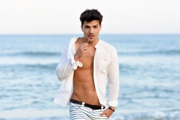 Man with sea background wearing unbuttoned shirt and showing sculpted abs after HD liposuction