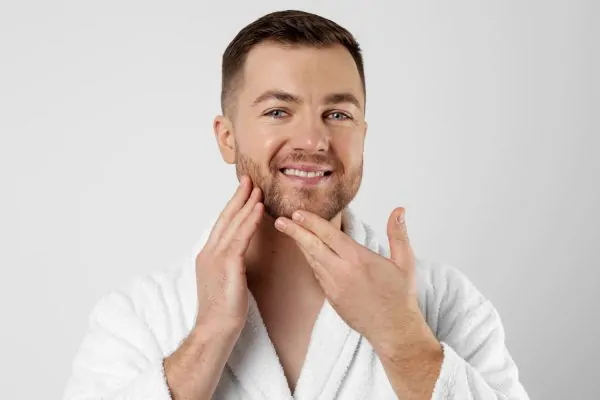 A man in a white bathrobe smiling and gently touching his face, showcasing smooth, natural-looking skin results after Botox treatment