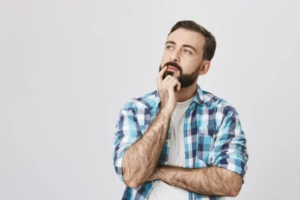 A thoughtful man stroking his beard and looking up, contemplating reconstructive surgery options and procedures.