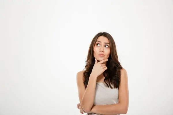 A woman in a casual tank top resting her finger on her chin with a curious, contemplative expression