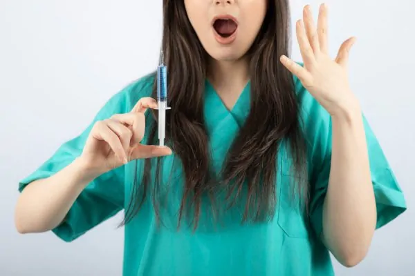 A woman in teal medical scrubs holding a syringe with a surprised expression, representing common questions and concerns about understanding peptides in skincare routines.