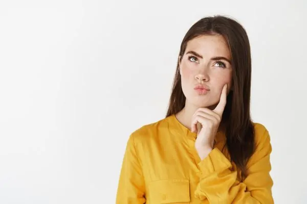 A young woman in a yellow blouse with a thoughtful, concerned expression, pondering the potential risks of returning to exercise too soon after neck liposuction