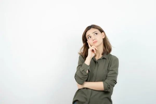 A young woman with a thoughtful expression, resting her finger on her cheek and looking upward, contemplating what Botox is and how it works