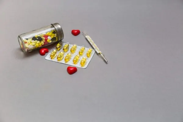 Assorted medications including pill bottle, blister pack of yellow capsules, thermometer, and red heart-shaped pills representing drug interactions