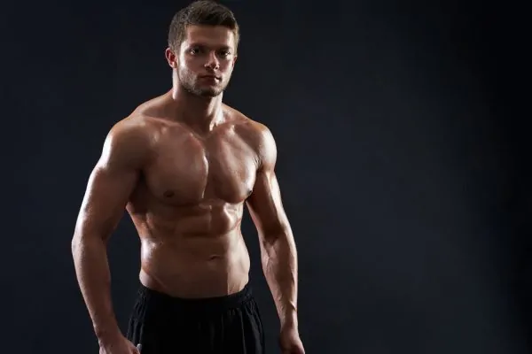Athletic man displaying sculpted chest and abdominal muscles against dark background, demonstrating muscle definition
