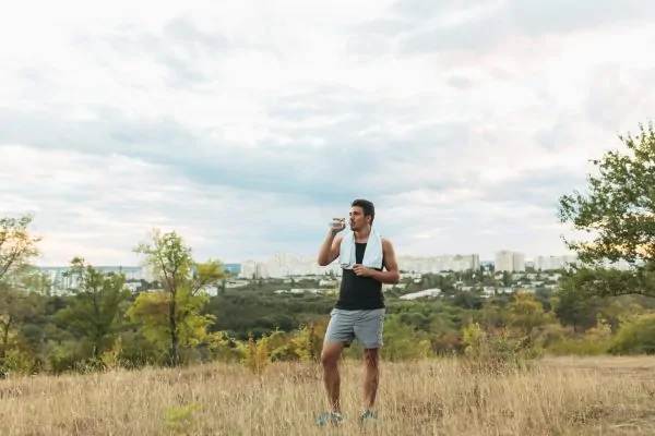 Athletic man drinking water outdoors after exercise, demonstrating healthy recovery and gradual return to physical activities following neck liposuction