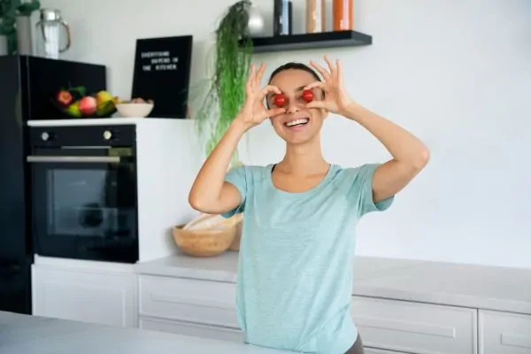 Happy woman holding cherry tomatoes in kitchen showcasing healthy eating after liposuction recovery