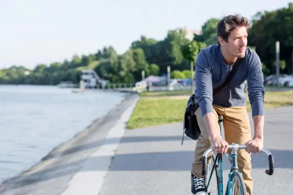 Man cycling along waterfront path, illustrating active lifestyle and return to normal exercise routines after neck liposuction recovery