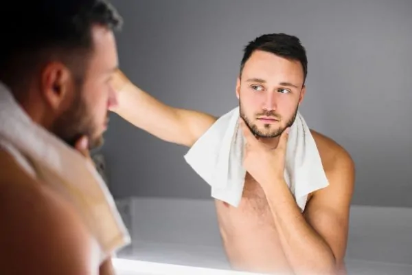 Man examining improved jawline and facial contours in mirror after PDO thread lift procedure