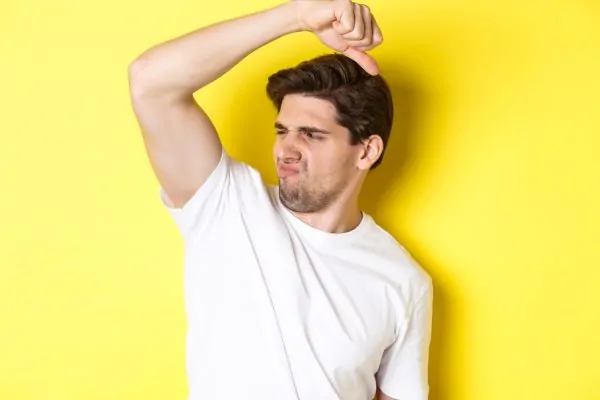 Man in a white t-shirt raising his arm and grimacing at his armpit odor, depicting the embarrassment of underarm smell that Botox treatment may help reduce