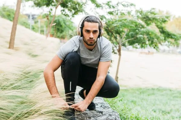 Man in athletic wear stretching outdoors with headphones, illustrating gradual return to exercise and normal activities after neck liposuction recovery