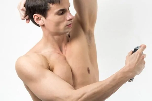 Man raising his arm and applying deodorant spray to his underarm, representing traditional odor control methods compared to how underarm Botox works to reduce sweating.
