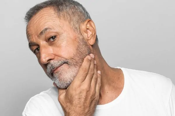 Older man touching his jawline and neck area showing signs of turkey neck sagging skin
