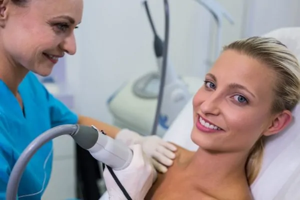 Patient smiling during liposuction consultation with medical professional holding treatment device