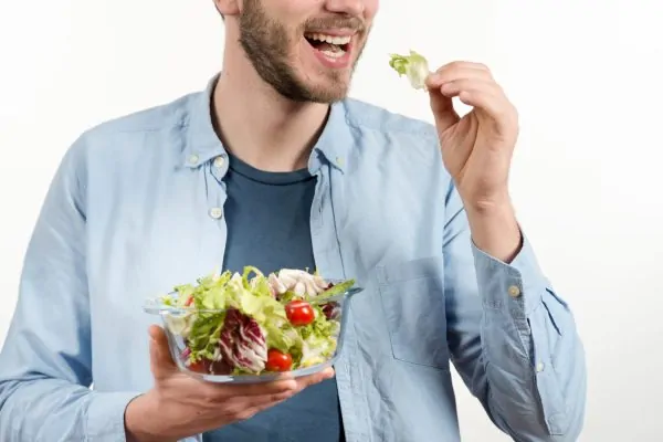 Smiling man enjoying a fresh vegetable salad, representing healthy eating habits to maximize tummy tuck results through positive lifestyle decisions.