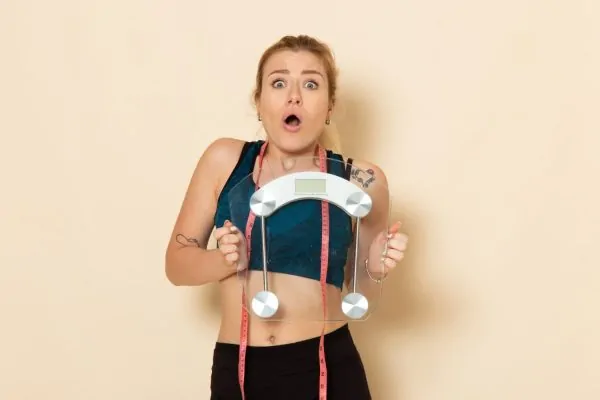 Surprised woman holding a scale and tape measure reacting to her tirzepatide weight loss results