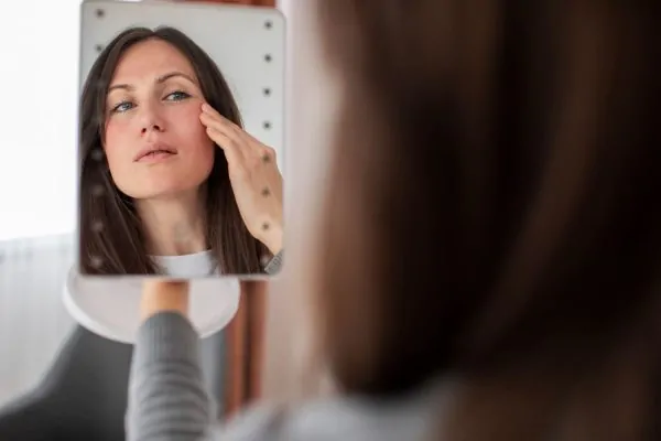 Woman examining facial features in mirror considering cosmetic filler treatment options