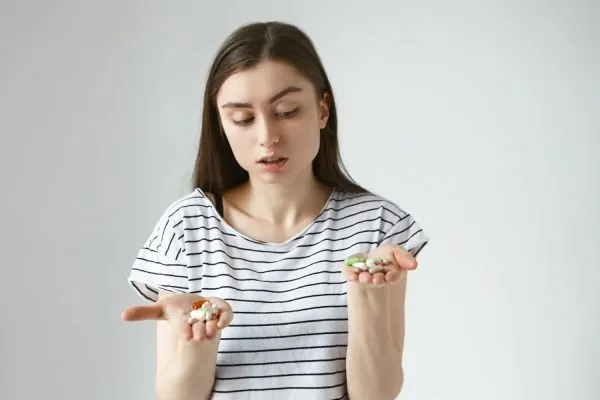 Woman in striped shirt comparing different pills and capsules in both hands, representing medication choices