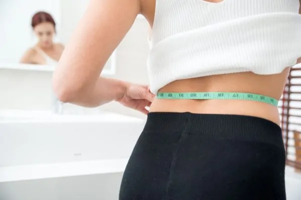 Woman measuring her waist in front of a mirror while tracking her progress toward maximum tirzepatide weight loss results