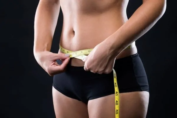 Woman measuring waist with tape measure illustrating abdominal contouring goals of tummy tuck procedure